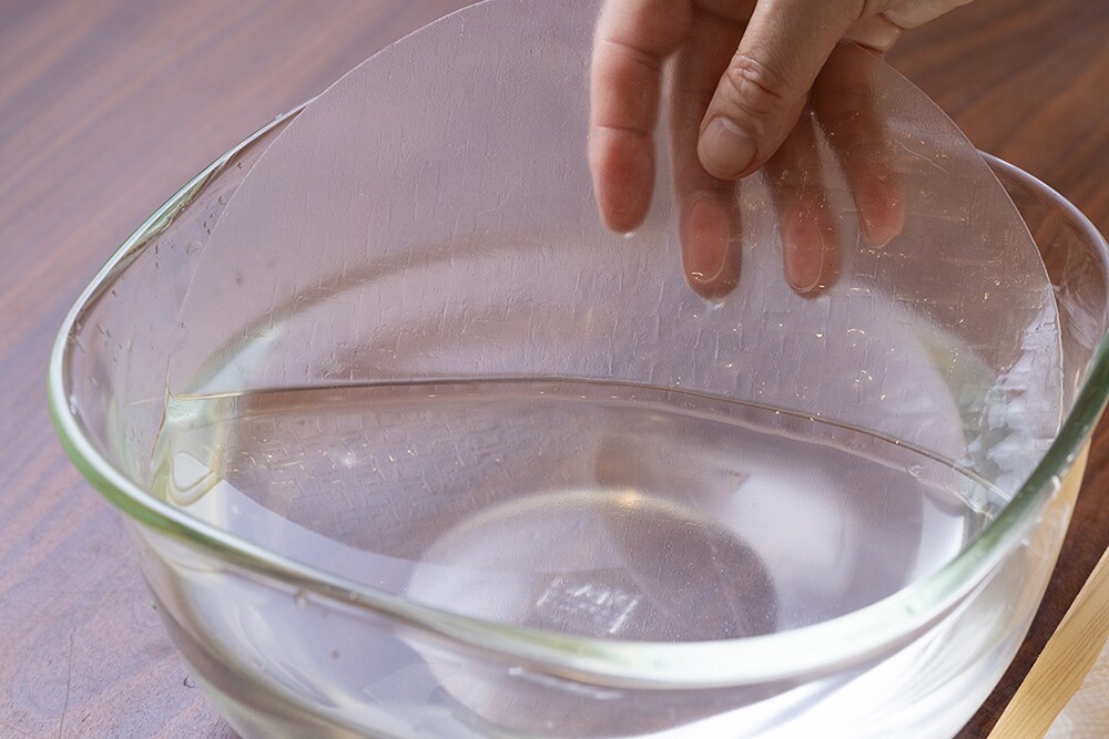 まな板の上にしっかりと湿らせたキッチンペーパーをのせ、ライスペーパーを1枚水にくぐらせて、その上にのせる。また、湿らせたキッチンペーパーをのせてはさみ、残りの3枚も同様にする。