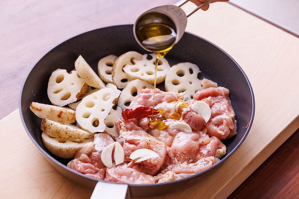 2、フライパンにれんこんと鶏肉を並べ入れ、にんにくと鷹の爪を上にのせたら、オリーブオイルを回し入れて中火にかけ、蓋をする。
