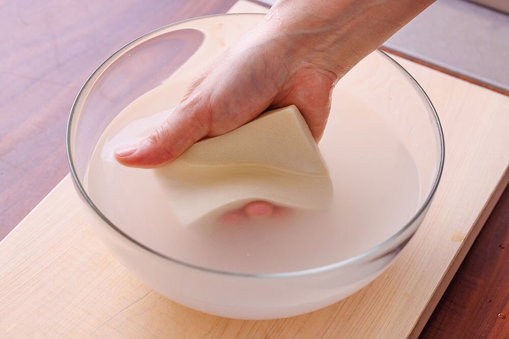 高野豆腐を水に浮かすように浸け、芯まで戻ったらスポンジを洗う要領でやさしく握って洗う。
